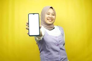 belle jeune femme musulmane asiatique souriante avec confiance et enthousiasme avec les mains tenant un smartphone, promotion de l'application, main de signe ok, bon travail, succès, isolé sur fond jaune photo
