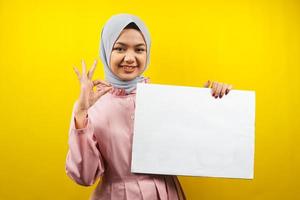 jolie jeune femme musulmane joyeuse tenant une bannière vide vierge, une pancarte, un tableau blanc, un panneau vierge, un panneau publicitaire blanc, présentant quelque chose dans l'espace de copie, promotion photo