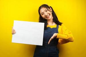 jolie et mignonne jeune femme joyeuse tenant une bannière vide vierge, une pancarte, un tableau blanc, un panneau vierge, un panneau publicitaire blanc, présentant quelque chose dans l'espace de copie, promotion photo