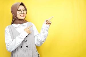 belle jeune femme musulmane asiatique souriante confiante, enthousiaste et joyeuse avec les mains pointant l'espace vide présentant quelque chose face à la caméra isolée sur fond jaune, concept publicitaire
