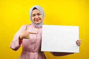 jolie jeune femme musulmane joyeuse tenant une bannière vide vierge, une pancarte, un tableau blanc, un panneau vierge, un panneau publicitaire blanc, présentant quelque chose dans l'espace de copie, promotion photo