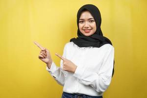 belle jeune femme musulmane asiatique souriante confiante, enthousiaste et joyeuse avec les mains pointant l'espace vide présentant quelque chose face à la caméra isolée sur fond jaune, concept publicitaire