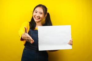 jolie et mignonne jeune femme joyeuse tenant une bannière vide vierge, une pancarte, un tableau blanc, un panneau vierge, un panneau publicitaire blanc, présentant quelque chose dans l'espace de copie, promotion photo