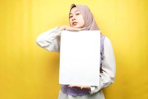 jolie jeune femme musulmane joyeuse tenant une bannière vide vierge, une pancarte, un tableau blanc, un panneau vierge, un panneau publicitaire blanc, présentant quelque chose dans l'espace de copie, promotion photo