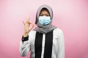 femme musulmane portant des masques médicaux, mouvement anti-virus corona, mouvement anti-covid-19, mouvement de santé utilisant des masques, avec les mains montrant le signe ok, bon travail, succès, victoire, isolé photo