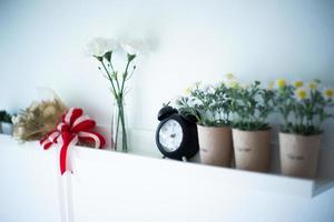 réveil vintage met sur l'étagère en bois blanc décorée par les fleurs en fleurs dans la poterie avec un arrière-plan flou de vase photo