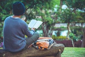 le jeune homme lisait un livre au parc. parmi les arbres naturels et le magnifique jardin fleuri