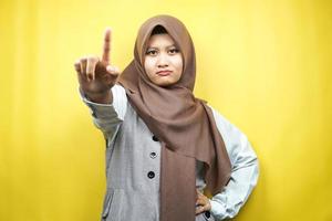 belle jeune femme musulmane asiatique affirmée, avec la main de signe numéro un, signe d'avertissement main à la caméra, isolée sur fond jaune