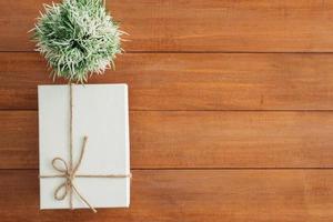 boîte-cadeau de vacances de noël et du nouvel an enveloppée de papier blanc et d'un noeud de ruban sur une table en bois - vue de dessus sur fond de table en bois. photo