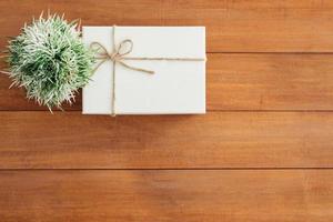 boîte-cadeau de vacances de noël et du nouvel an enveloppée de papier blanc et d'un noeud de ruban sur une table en bois - vue de dessus sur fond de table en bois. photo
