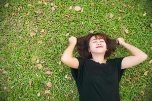 jeune femme asiatique allongée sur l'herbe verte écoutant de la musique dans le parc avec une émotion froide. jeune femme se reposant sur l'herbe avec sa liste de lecture musicale. activité de plein air dans le concept de parc. photo