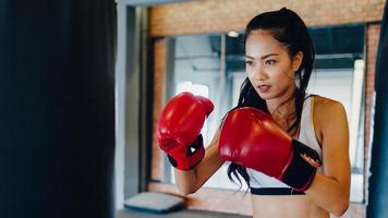Jeune femme d'Asie kickboxing exercice sac de boxe dur combattant féminin pratique la boxe dans la classe de remise en forme de gym. activité récréative sportive, entraînement fonctionnel, concept de mode de vie sain. photo
