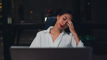 Jeune femme d'affaires chinoise millénaire travaillant tard dans la nuit avec un problème de recherche de projet sur un ordinateur portable dans la salle de réunion d'un petit bureau moderne. concept de syndrome d'épuisement professionnel des personnes d'asie.