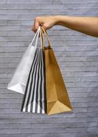 maquette d'emballage écologique en gros plan sur un fond gris brique. sac kraft à rayures noires et blanches, blanc, artisanal dans la main d'une femme. concept d'achat en ligne, livraison, commandes en ligne. photo