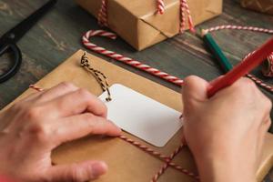 Femme écrivant une étiquette-cadeau et attachez-la au cadeau de Noël sur une table en bois photo