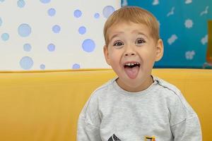 beau et joyeux petit garçon fait des grimaces dans un café à une table sur l'aire de restauration du centre commercial. achats. photo