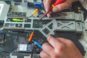 un homme répare un ordinateur, soude une carte, répare l'électronique et les technologies modernes photo