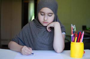 enfant fille en hijab dessine à la table photo