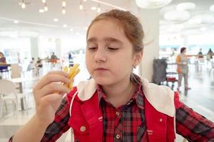 adolescente affamée mangeant des frites sur l'aire de restauration du centre commercial. aliments malsains. photo