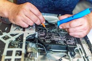 un homme répare un ordinateur, soude une carte, répare l'électronique et les technologies modernes photo