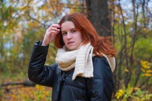 portrait d'une fille souriante aux cheveux roux dans une veste redresse ses cheveux avec ses mains. dans le contexte de la nature automnale, le concept d'émotions humaines photo