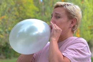 une femme aux cheveux courts a gonflé un gros ballon blanc argenté dans la nature dans le parc photo