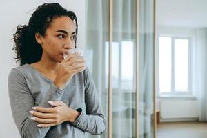 jeune femme noire buvant de l'eau pendant qu'elle passe du temps à la maison