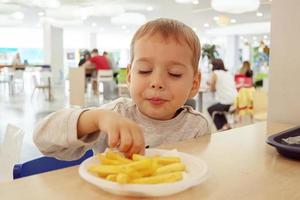 petit enfant mangeant des frites assis à une table sur l'aire de restauration du centre commercial. aliments malsains. photo