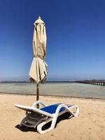 chaise longue élégante dans le sable jaune au soleil transat sur la plage en été sous le ciel ouvert photo