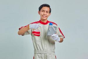 Portrait d'un bel homme joyeux portant un uniforme de mécanicien montrant une bouteille en plastique d'huile moteur sur fond gris photo