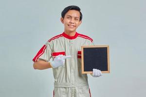Portrait d'un jeune mécanicien joyeux en uniforme pointant sur un tableau blanc avec le doigt sur fond gris