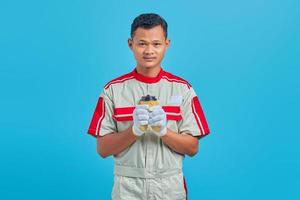 Portrait de jeune mécanicien asiatique souriant portant une tasse de café à la main sur fond bleu