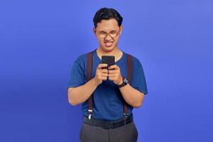 Jeune homme asiatique en colère regardant un téléphone mobile isolé sur fond violet photo