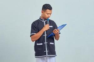 Portrait d'un jeune homme asiatique confus portant un uniforme de karaté tenant un presse-papiers et un stylo avec un stylo photo