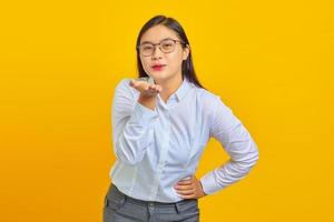 Portrait d'une belle jeune femme d'affaires avec un visage confiant tenant des paumes envoyant un baiser aérien à son petit ami sur fond jaune photo