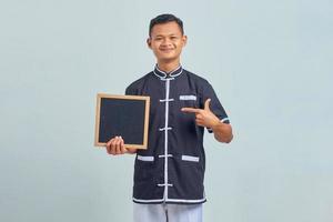 Portrait d'un jeune homme asiatique joyeux portant un uniforme de karaté pointant sur un tableau blanc avec le doigt sur fond gris photo