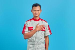 Portrait de jeune mécanicien asiatique souriant avec des paumes sur la poitrine sur fond bleu photo