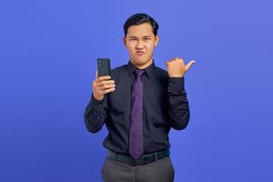 surpris beau jeune homme d'affaires pointant vers la salle de copie et tenant un smartphone sur fond violet photo