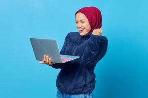 photo d'une femme asiatique excitée regardant un e-mail entrant sur un ordinateur portable sur fond bleu