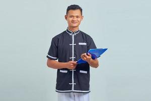 Portrait d'un jeune homme asiatique souriant portant un uniforme de karaté tenant un presse-papiers sur fond gris photo