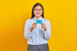 Portrait de jeune femme asiatique souriante montrant une carte de crédit sur fond jaune photo