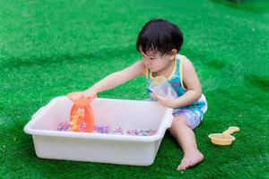 petit garçon d'âge préscolaire utilisant la main pour jouer des perles d'eau ou des perles arc-en-ciel dans un bassin blanc avec un cône de turbine orange. bébé de 2 ans.