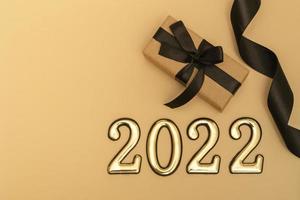 nouvel an 2022. vue de dessus maquette du nouvel an sur fond beige ruban noir, coffret cadeau, nombres dorés et paillettes multicolores. mise en page de cartes postales photo