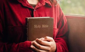 une adolescente vêtue d'un chemisier rouge prie pour la bénédiction de Dieu. avoir une vie meilleure une femme embrasse la bible avec une bible par la fenêtre, belle vue, une crise dans la vie chrétienne photo