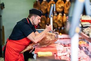 Boucher désossant un jambon dans une boucherie moderne photo