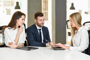 femme d'affaires blonde expliquant avec un ordinateur portable à un jeune couple souriant. photo