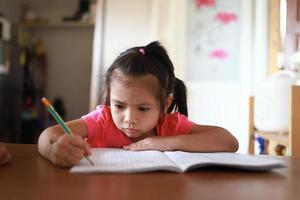 une jolie fille asiatique fait ses devoirs dans sa maison pendant la journée photo