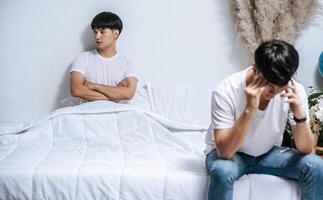 deux jeunes hommes étaient en colère sur le lit et l'autre était assis au bord du lit et était stressé. photo