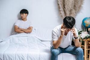 deux jeunes hommes étaient en colère sur le lit et l'autre était assis au bord du lit et était stressé. photo