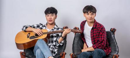 deux jeunes hommes étaient assis sur une chaise et jouaient de la guitare. photo